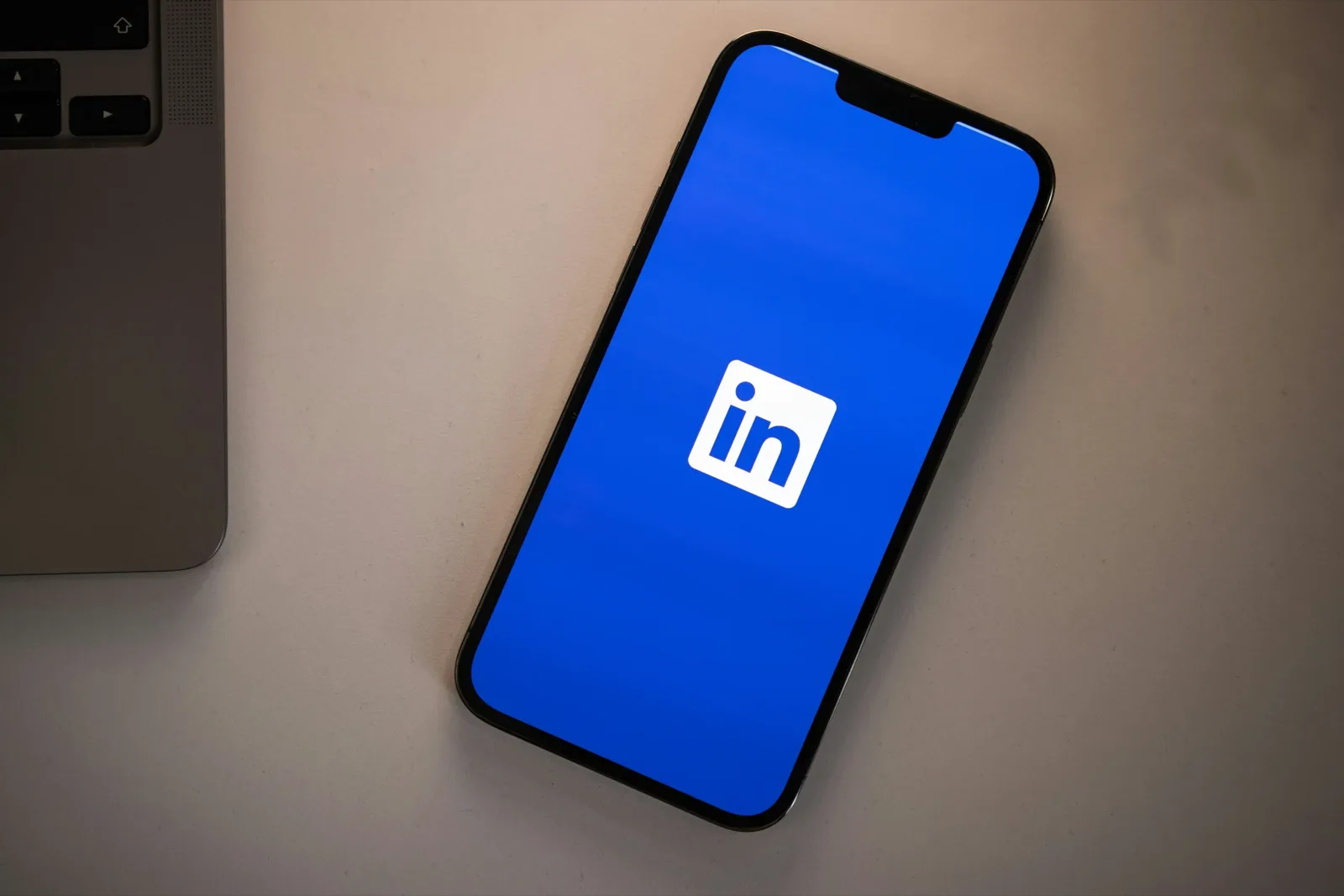 Smartphone met het blauwe LinkedIn-logo op het scherm, naast een laptop op een licht bureau